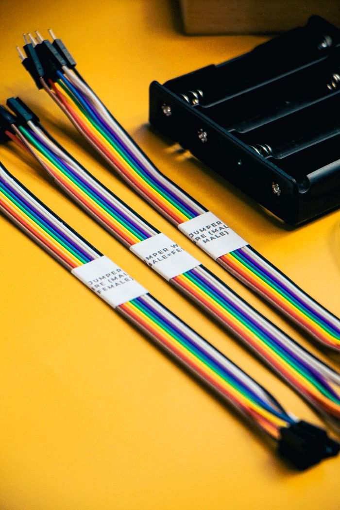 services-03 Vibrant multi-colored wires and battery pack on yellow background, ideal for robotics projects.