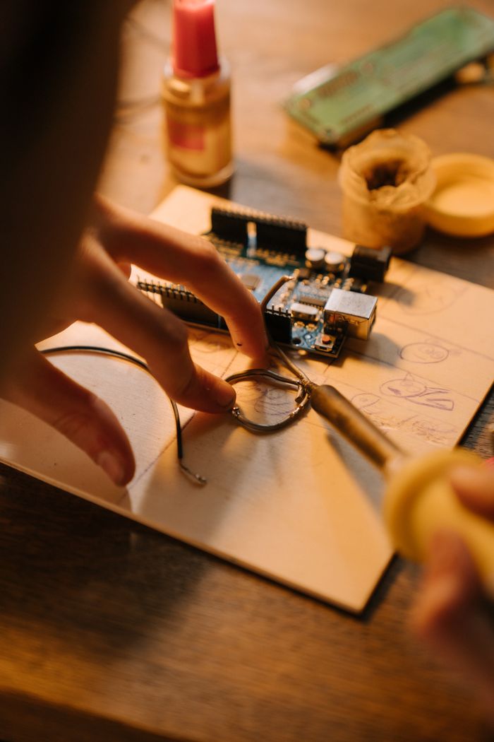 about-us-01 Hands intricately repairing a circuit board with a soldering iron under warm lighting.
